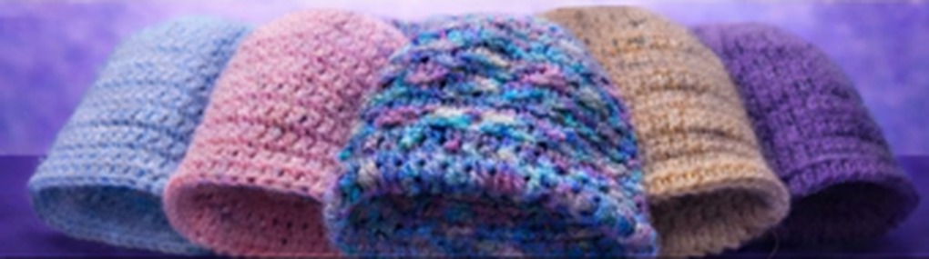 Row of five handmade crochet chemo hats in blue, pink, variegated, tan and purple